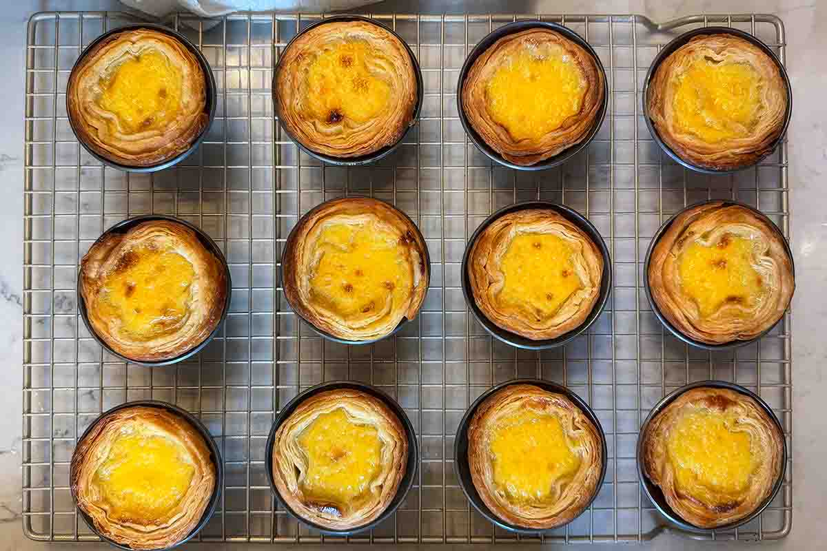 12 Portuguese custard pastries cooling on a wire rack.