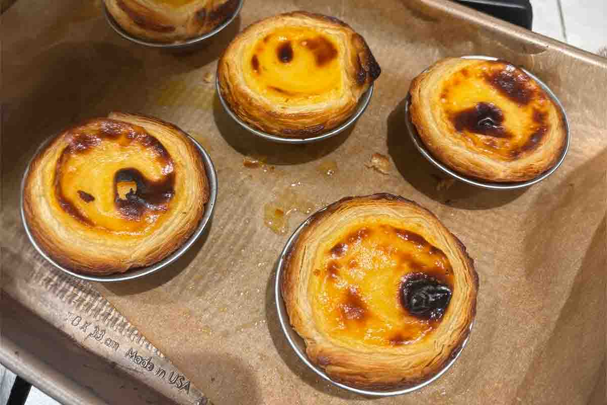 Four Porrtuguese custard cups cooling on a parchment-lined cooking sheet.