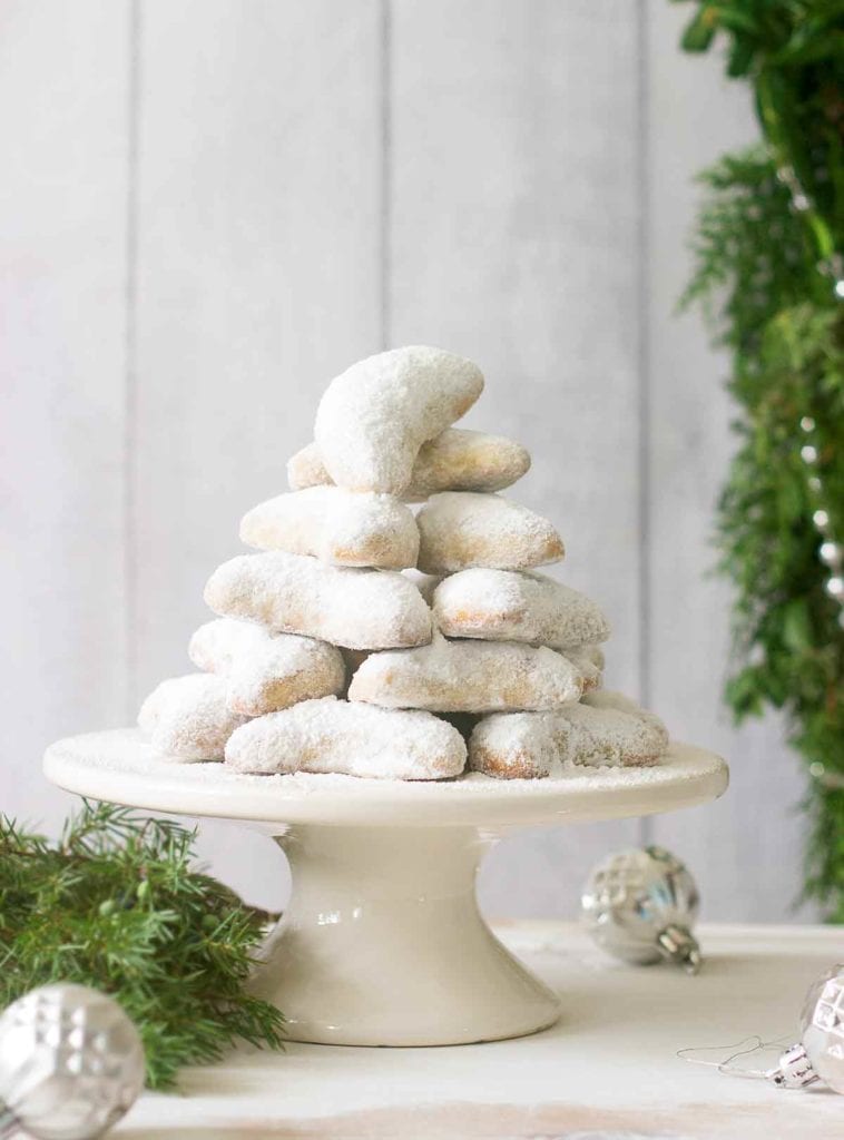 Walnut crescents stacked on a white stand with Christmas decorations and greenery around them.
