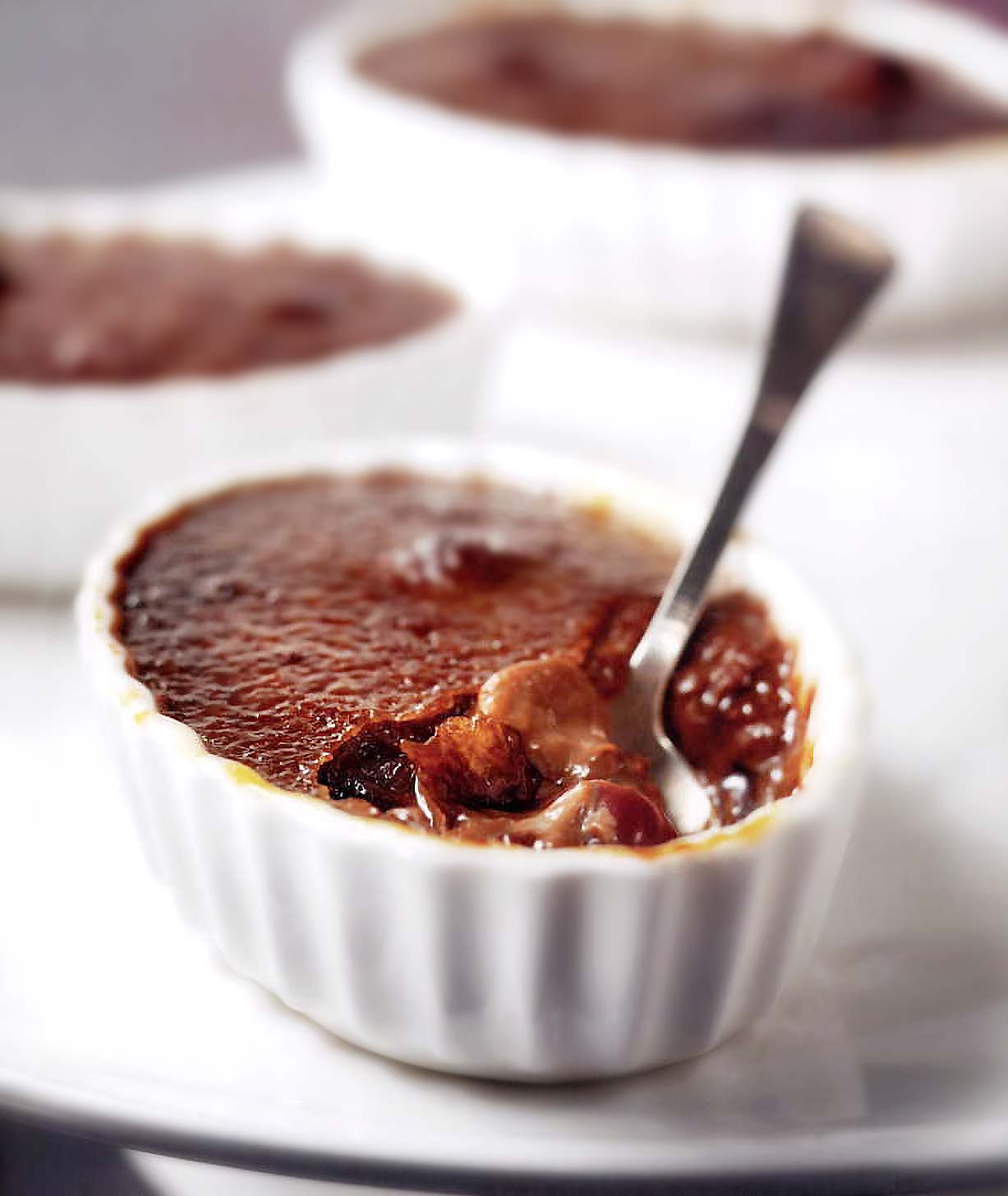 A single cherry and chocolate crème brûlée with a spoon resting in it.