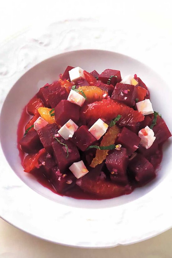 A white bowl filled with a beet salad with feta and orange and sliced mint leaves
