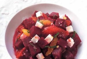 A white bowl filled with a beet salad with feta and orange and sliced mint leaves