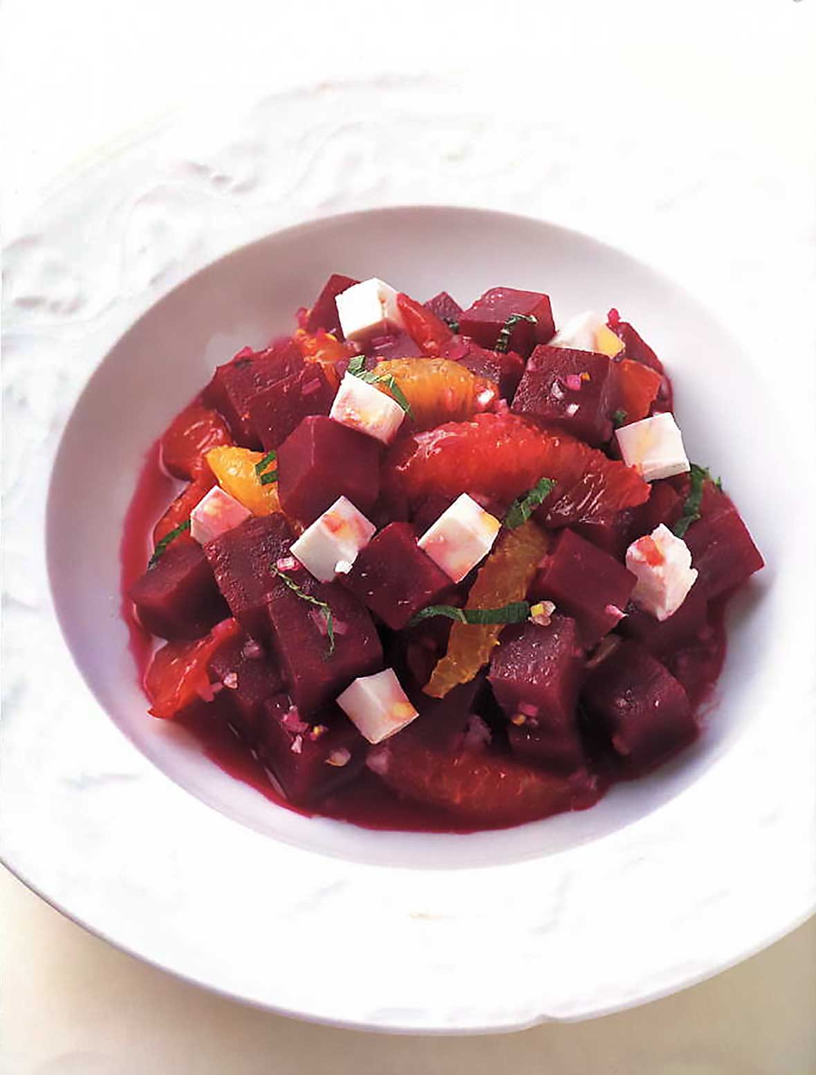 A white bowl filled with a beet salad with feta and orange and sliced mint leaves