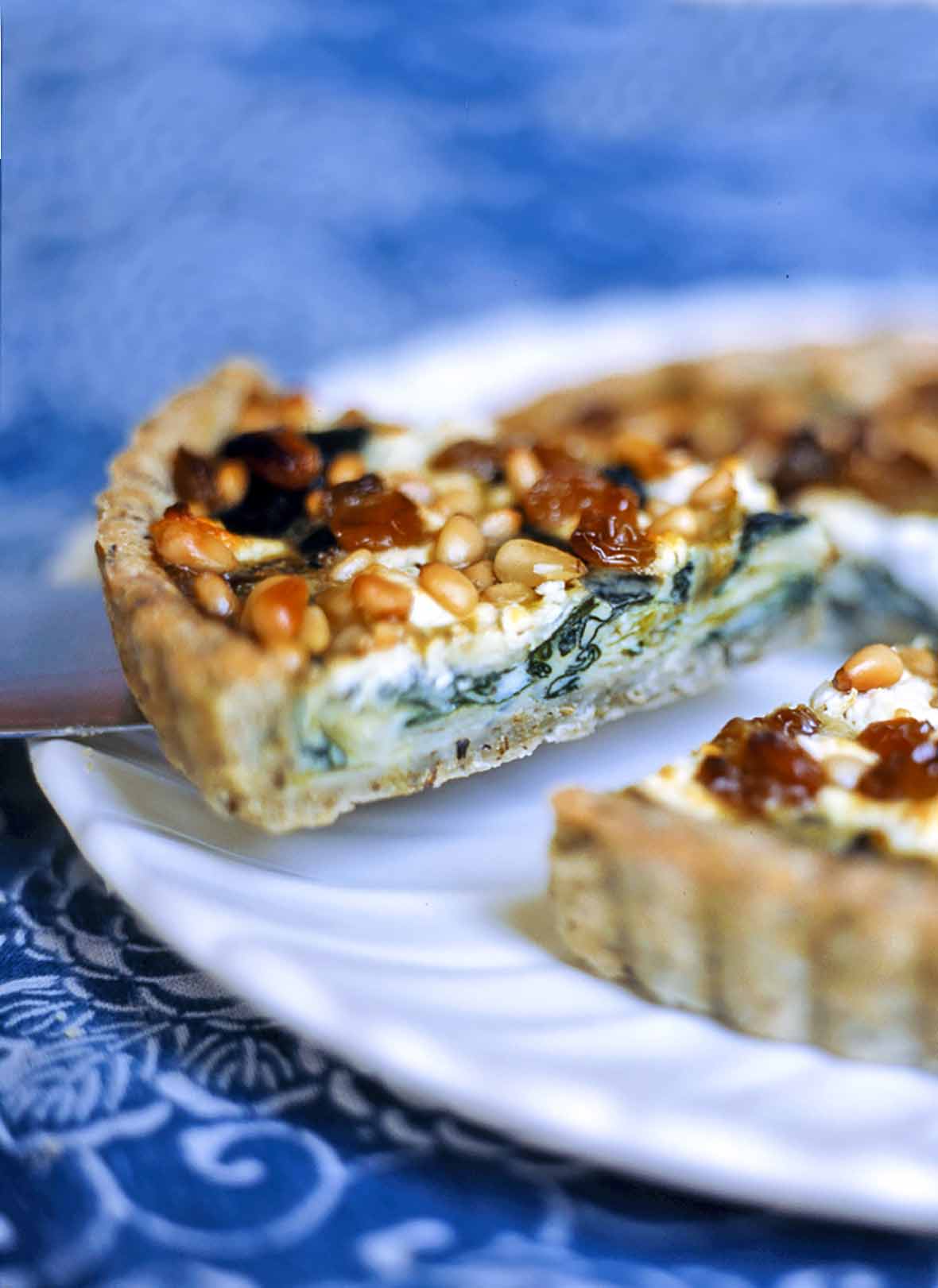 A swiss chard, leek, and goat cheese tart on a white platter with one slice being cut.