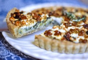 A swiss chard, leek, and goat cheese tart on a white platter with one slice being cut.