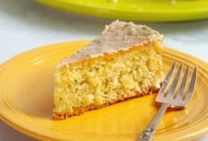 A slice of coconut lime macadamia cake on a yellow plate with a fork resting beside it