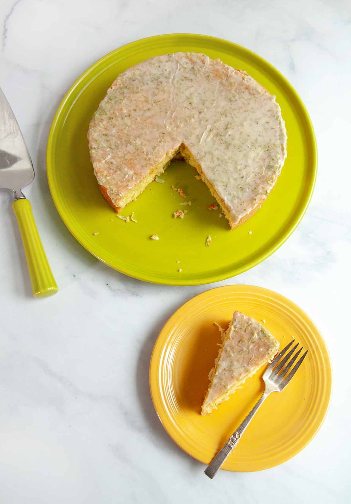 A coconut lime macadamia cake on a green platter with one slice cut out and placed on a yellow plate
