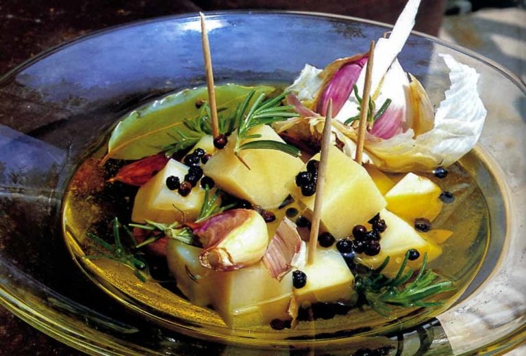 Marinated Idiazábal cheese chunks, garlic, and rosemary on a glass plate