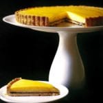 Meyer lemon tart on a white cake stand and a slice of tart on a small plate, black background