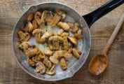 A skillet filled with mushrooms with garlic and sherry, sprinkled with parsley, and a wooden spoon resting beside it.