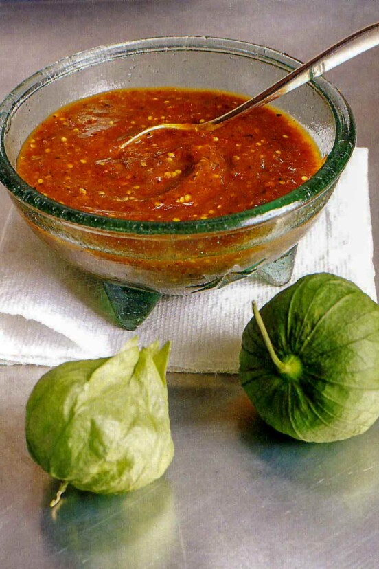 Smoky chipotle salsa with pan-roasted tomatillos in a glass bowl on a towel, two tomatillo in front