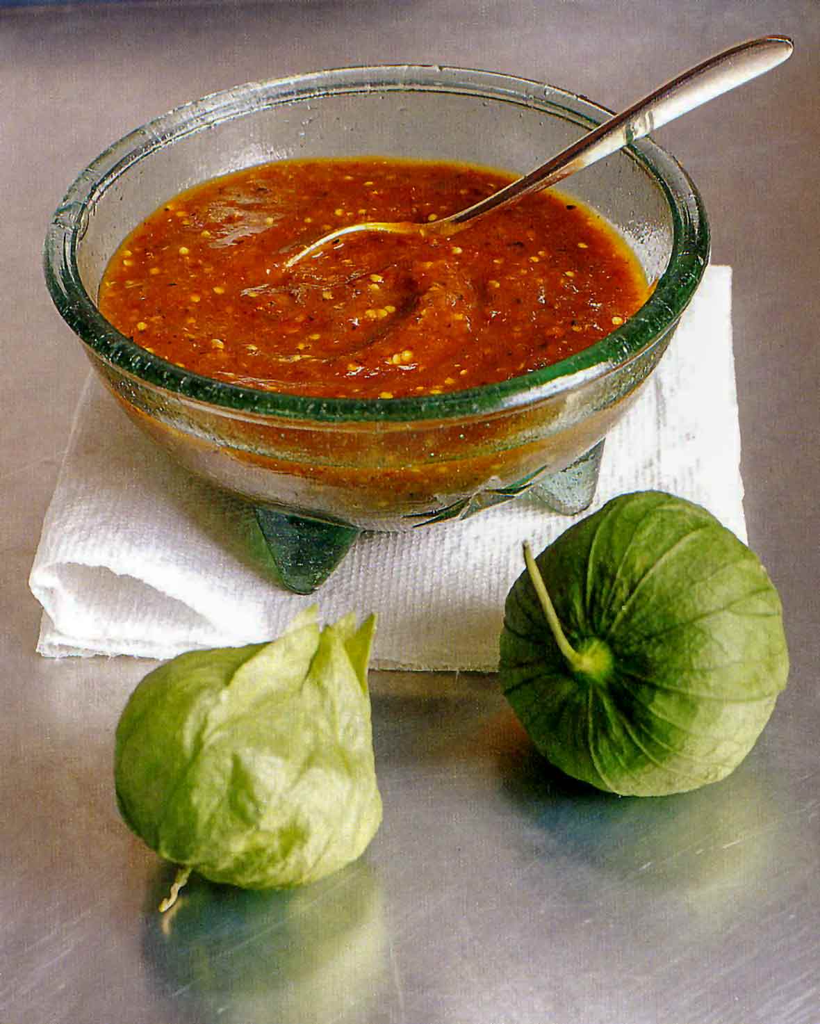 Smoky chipotle salsa with pan-roasted tomatillos in a glass bowl on a towel, two tomatillo in front