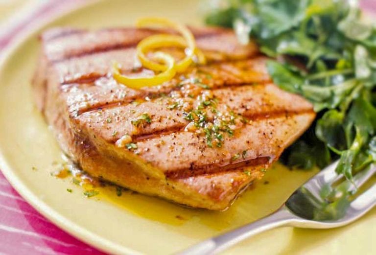 A grilled tuna steaks with spiced vinaigrette with lemon zest on top, a salad on the side