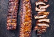 Two racks of barbecued baby back ribs, and a third rack cut into individual ribs, resting on a knife.