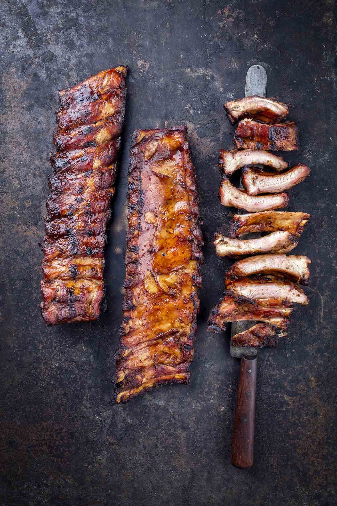 Two racks of barbecued baby back ribs, and a third rack cut into individual ribs, resting on a knife.