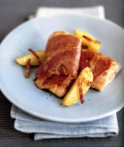 Two fillet of Portuguese trout wrapped in ham then cooked, on the side slices of peaches on a plate
