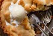A classic apple pie with one-quarter missing, topped with a scoop of ice cream, and three forks in the empty pie spot.