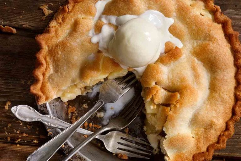 A classic apple pie with one-quarter missing, topped with a scoop of ice cream, and three forks in the empty pie spot.
