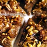 Lamb kibbeh cut into wedges topped with caramelized onions and toasted pine nuts