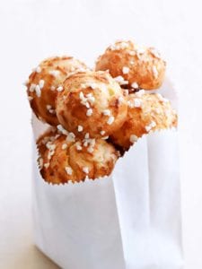 Several chouquettes, or cream puffs with pearl sugar in a paper bag.