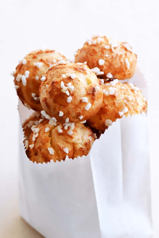 Several chouquettes, or cream puffs with pearl sugar in a paper bag.