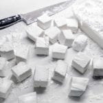 Cubes of homemade marshmallows on a white surface with a chef's knife lying beside.