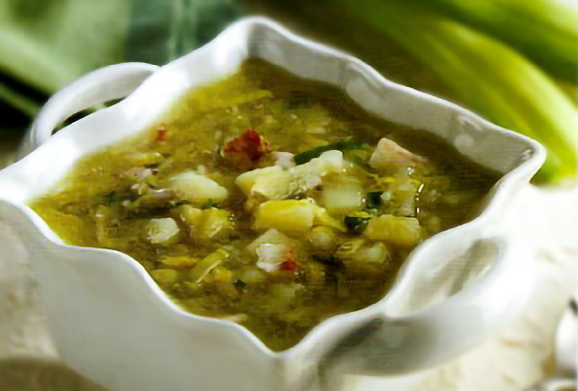 A square white bowl of leek and potato soup with bacon