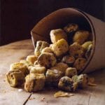 Paper cone with crispy fried okra bites spilling out on top a wooden board