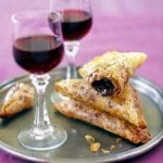 Crispy chocolate-filled pastry triangles and two glasses of dessert wine on a silver tray