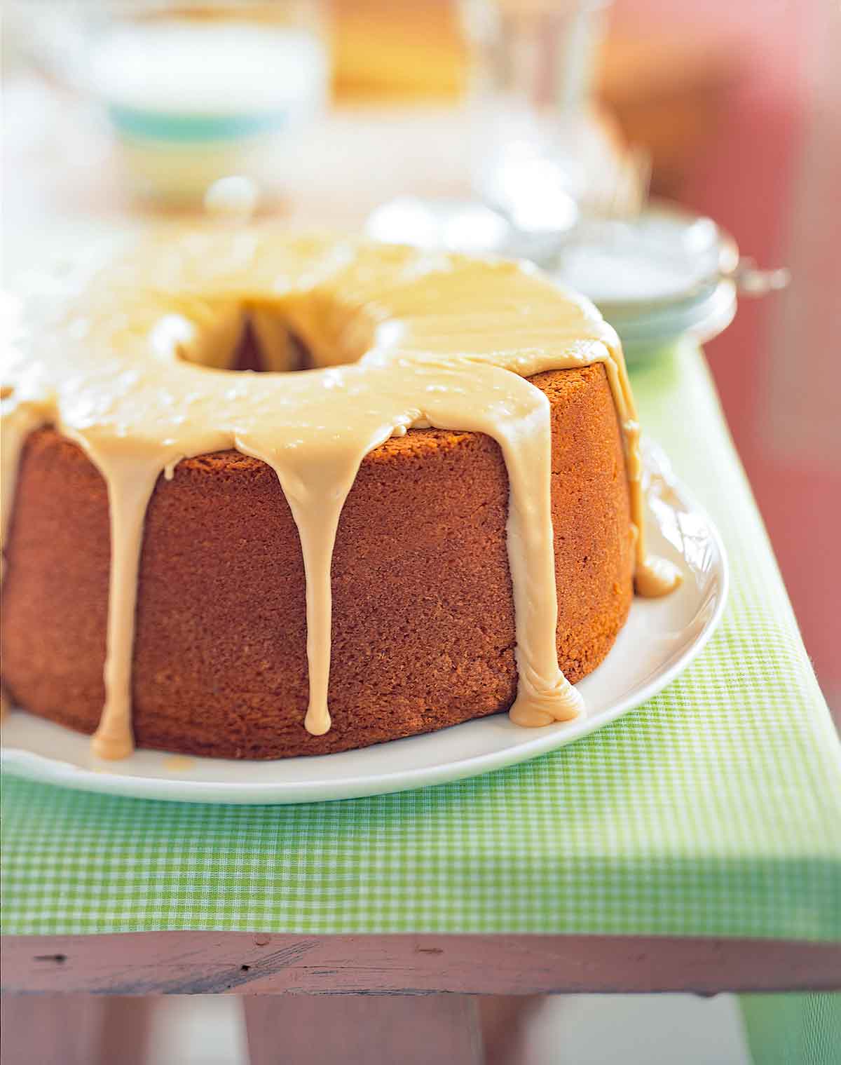 A frosted brown sugar pound cake on a white plate on a cloth-covered picnic table.