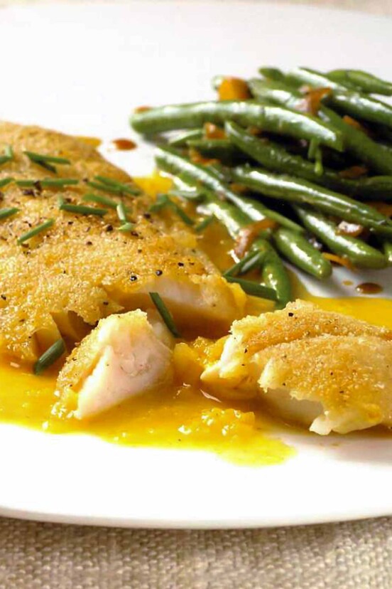 A white plate with a serving of crispy rock cod with citrus sauce and a side of green beans.