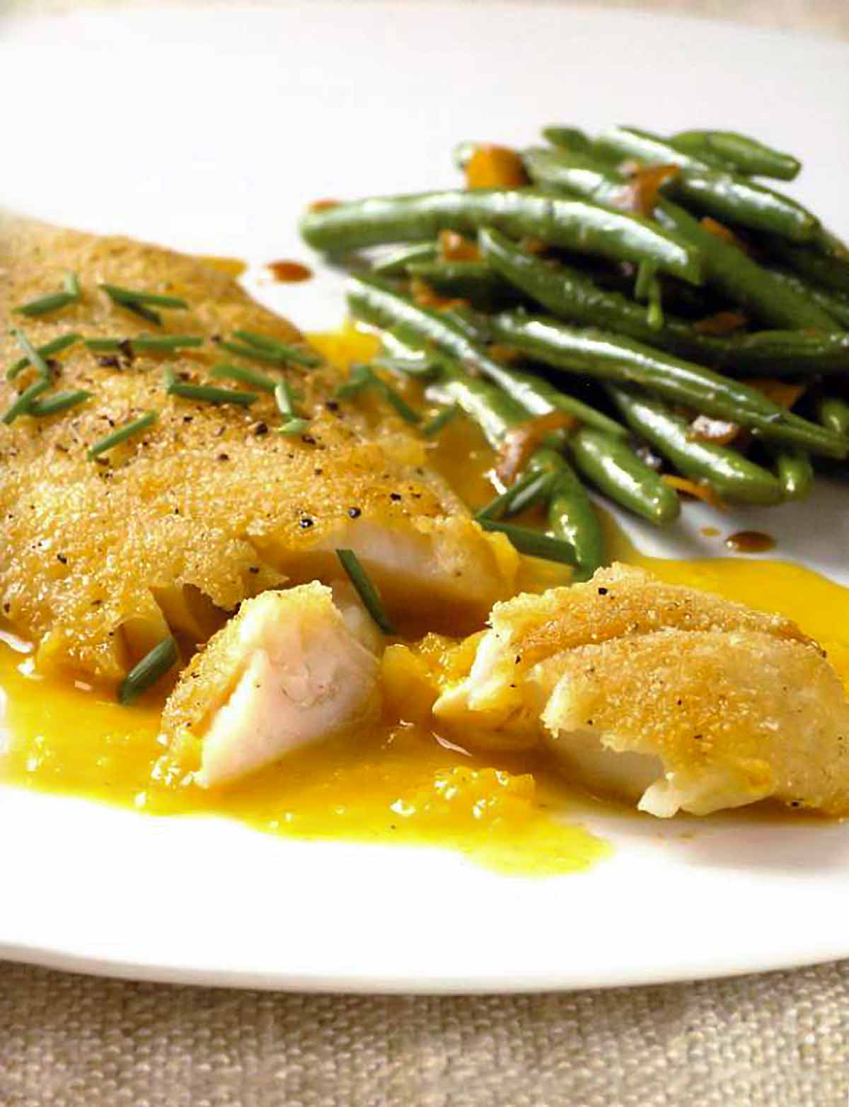 A white plate with a serving of crispy rock cod with citrus sauce and a side of green beans.