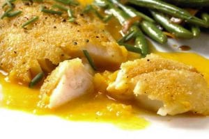 A white plate with a serving of crispy rock cod with citrus sauce and a side of green beans.