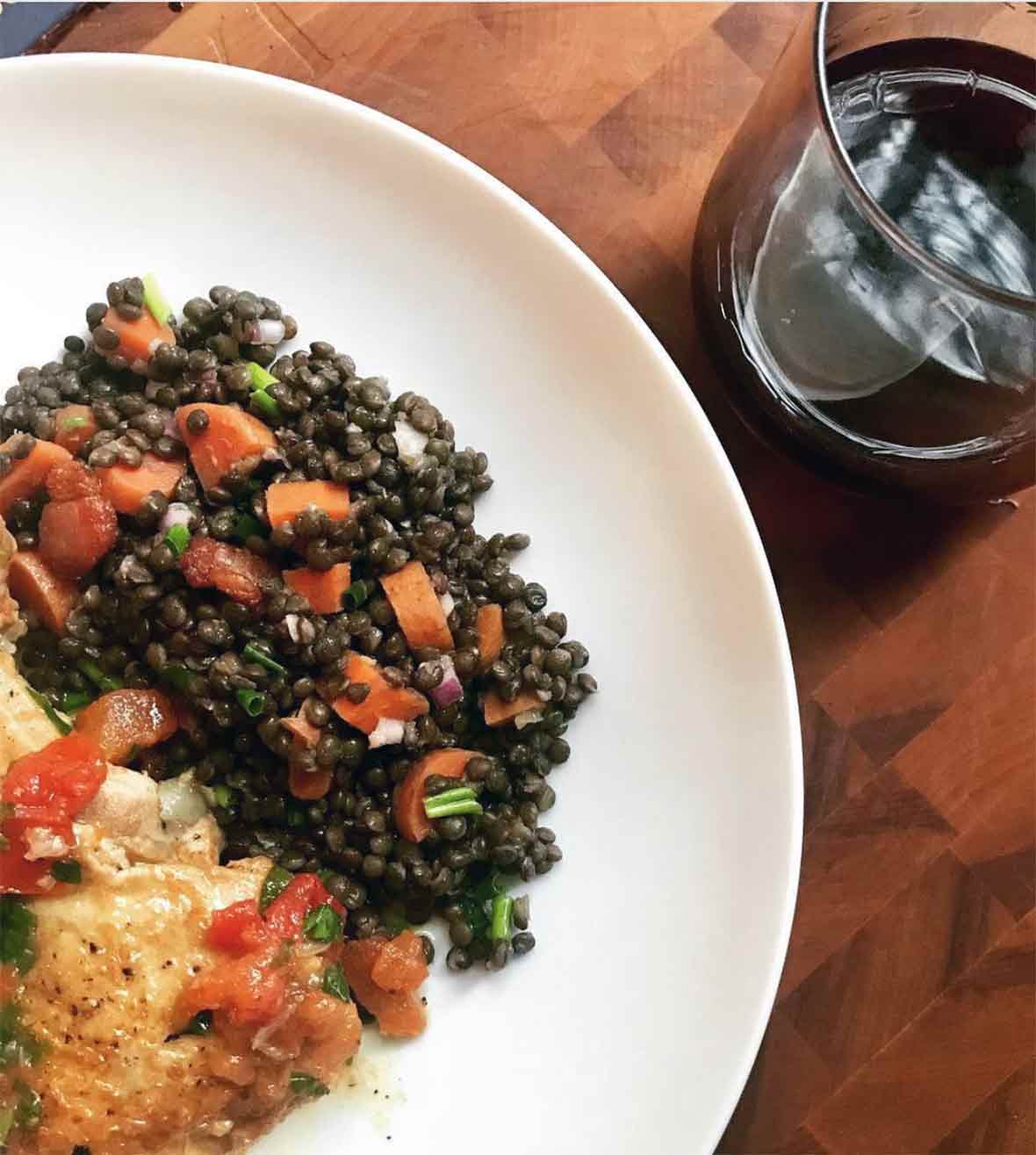 White plate with warm lentil salad and a glass of wine