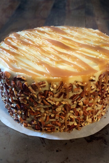 An apple spice cake with caramel buttercream and a pecan crusted sides on a parchment round.