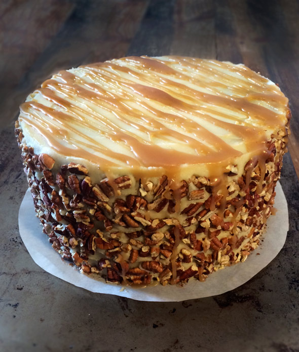An apple spice cake with caramel buttercream and a pecan crusted sides on a parchment round.