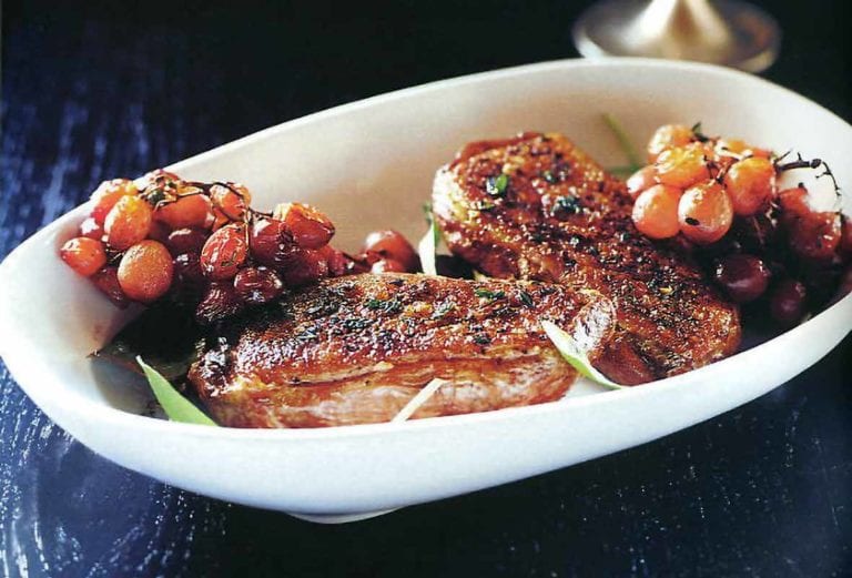 Grilled duck breasts with roasted grapes and potato-bacon gratin on a white plate on black background