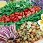 Platter of nicoise salad with slice tuna, roasted potatoes, sliced eggs, green beans, tomatoes, and greens