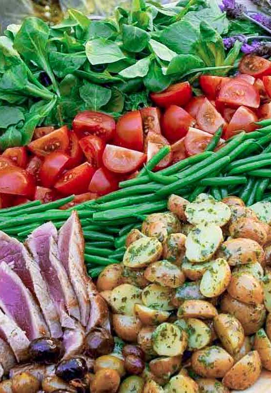 Platter of nicoise salad with slice tuna, roasted potatoes, sliced eggs, green beans, tomatoes, and greens