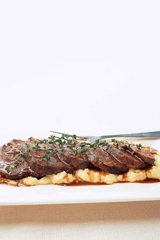 A sliced beef braised in Barolo, garnished with thyme sprigs, on a bed of mashed potatoes.