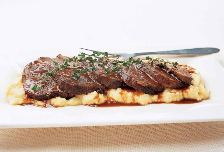 A sliced beef braised in Barolo, garnished with thyme sprigs, on a bed of mashed potatoes.