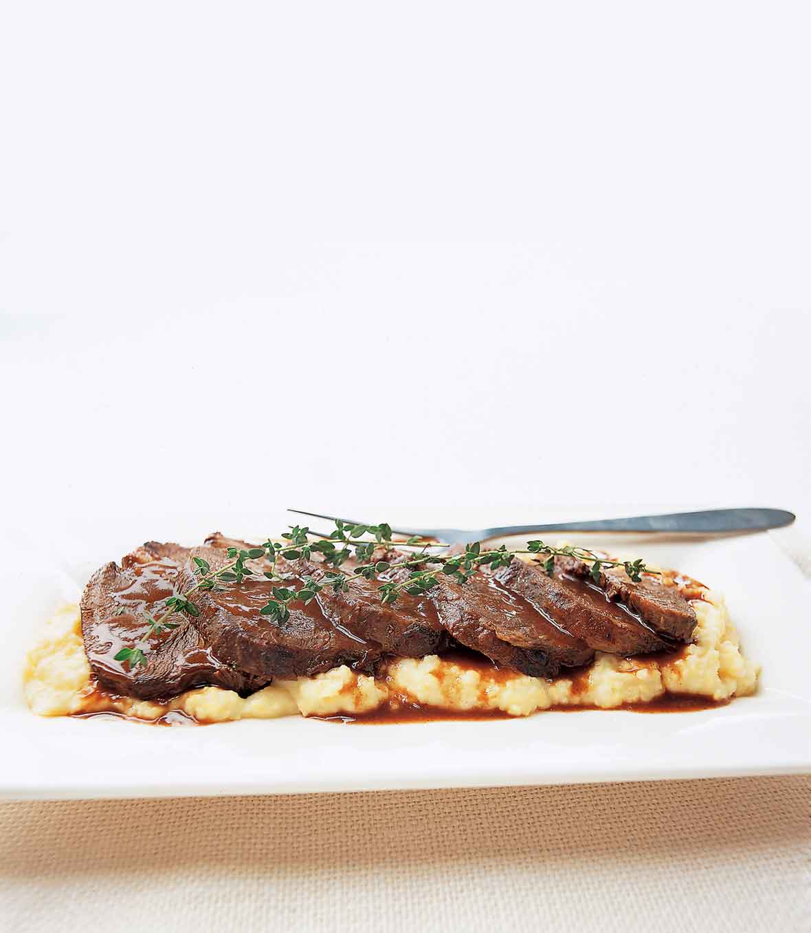 A sliced beef braised in Barolo, garnished with thyme sprigs, on a bed of mashed potatoes.