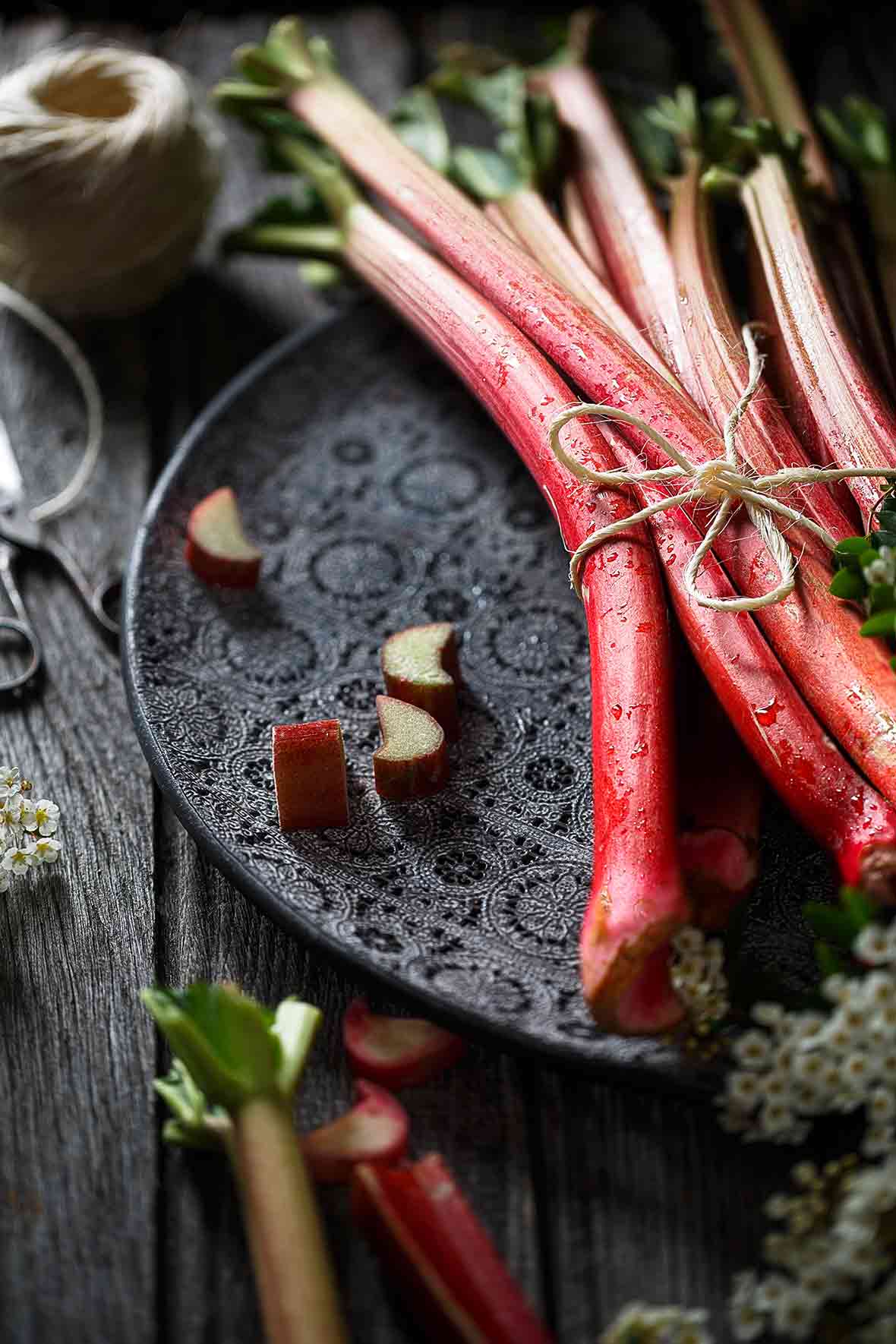 A bunch of rhubarb stalks tied together with twine on a black platter for use in rhubarb with berries and candied ginger