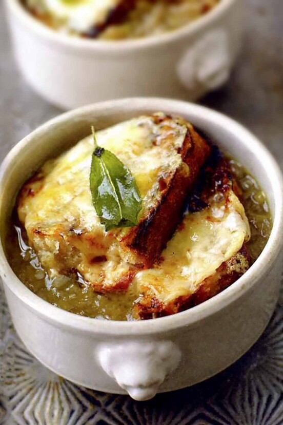 Bowl of onion soup with two slices of bread covered with melted cheese and a sage leaf