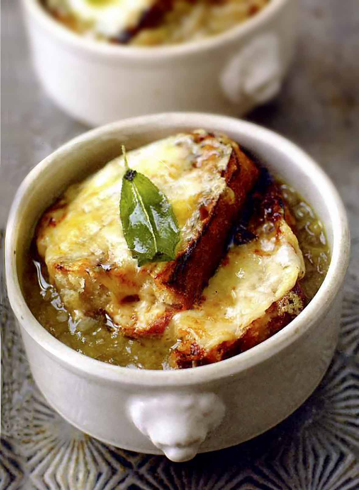 Bowl of onion soup with two slices of bread covered with melted cheese and a sage leaf