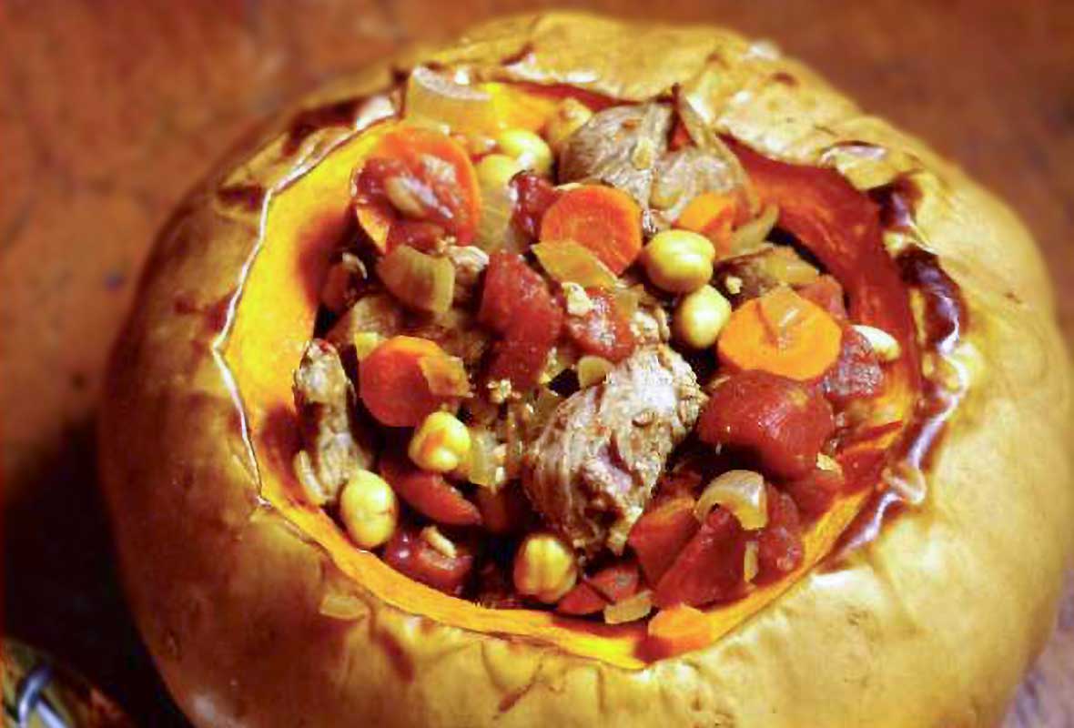 Lamb tagine in a whole roasted pumpkin with the top removed; inside chunks of lamb, pumpkin, tomato, chickpeas