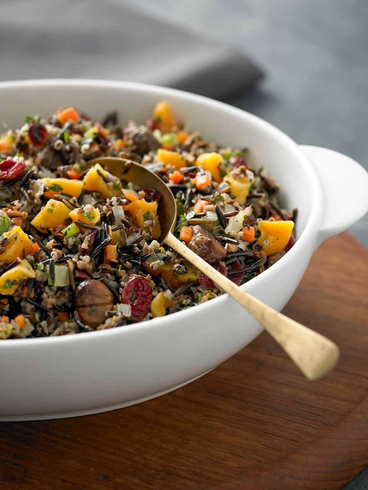 A white bowl of wild rice, roasted chestnuts, and cranberries with a gold spoon resting inside..