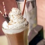 Tall glass filled with a chocolate milkshake, topped with whipped cream, chocolate shavings, three straws