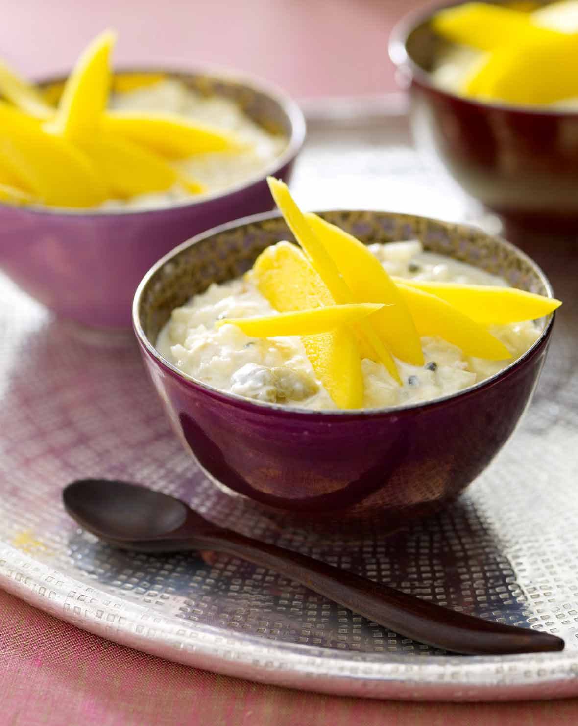 Three bowls of Indian rice pudding parfait with mango slices on top on a platter