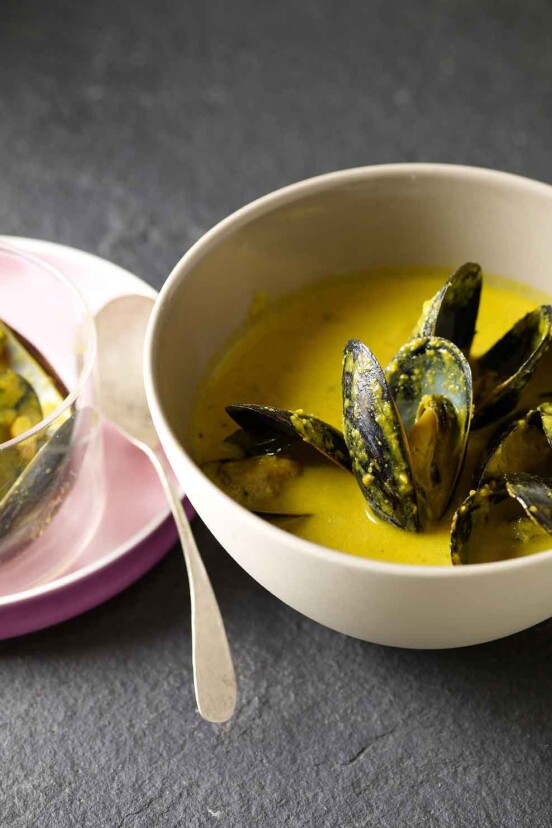 Bowl of saffron mussel stew with a yellow broth, a plate with shells to the left
